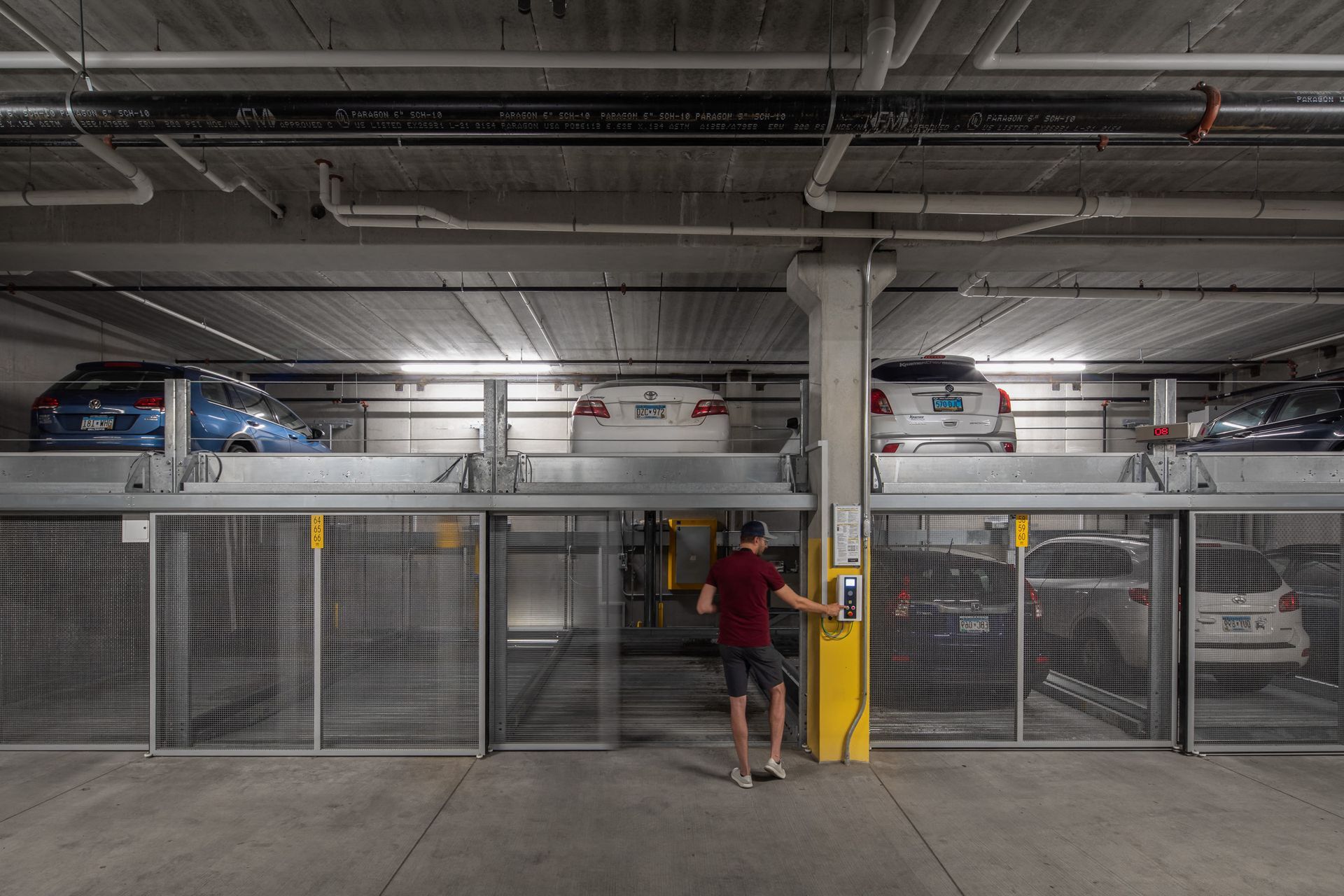 Underground parking garage with cars on two levels and a man at a payment terminal.