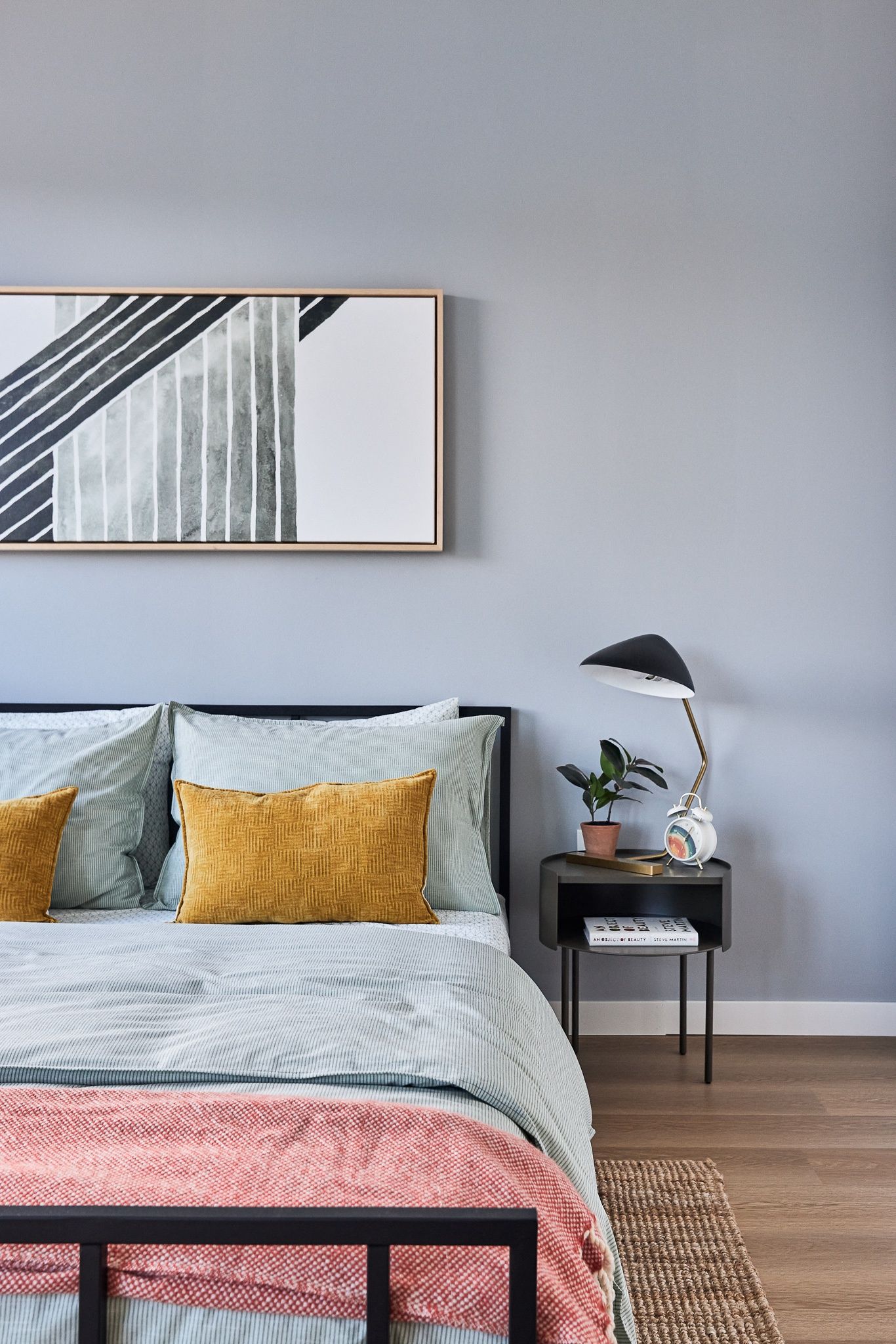 Modern bedroom with blue-gray walls, bed, and side table with lamp.