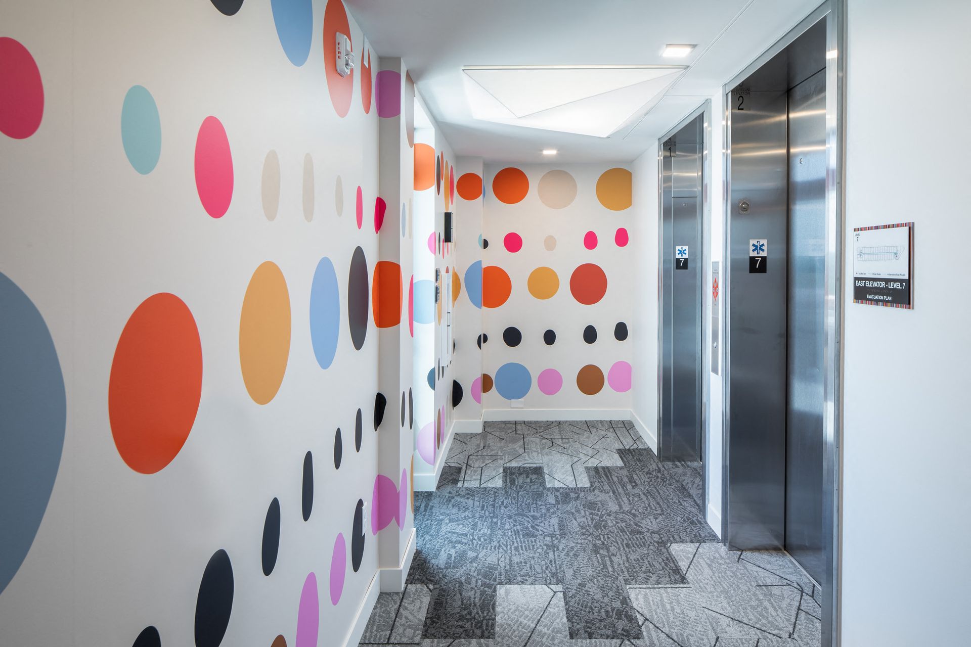 Interior hallway with a colorful polka-dot mural and elevator doors.