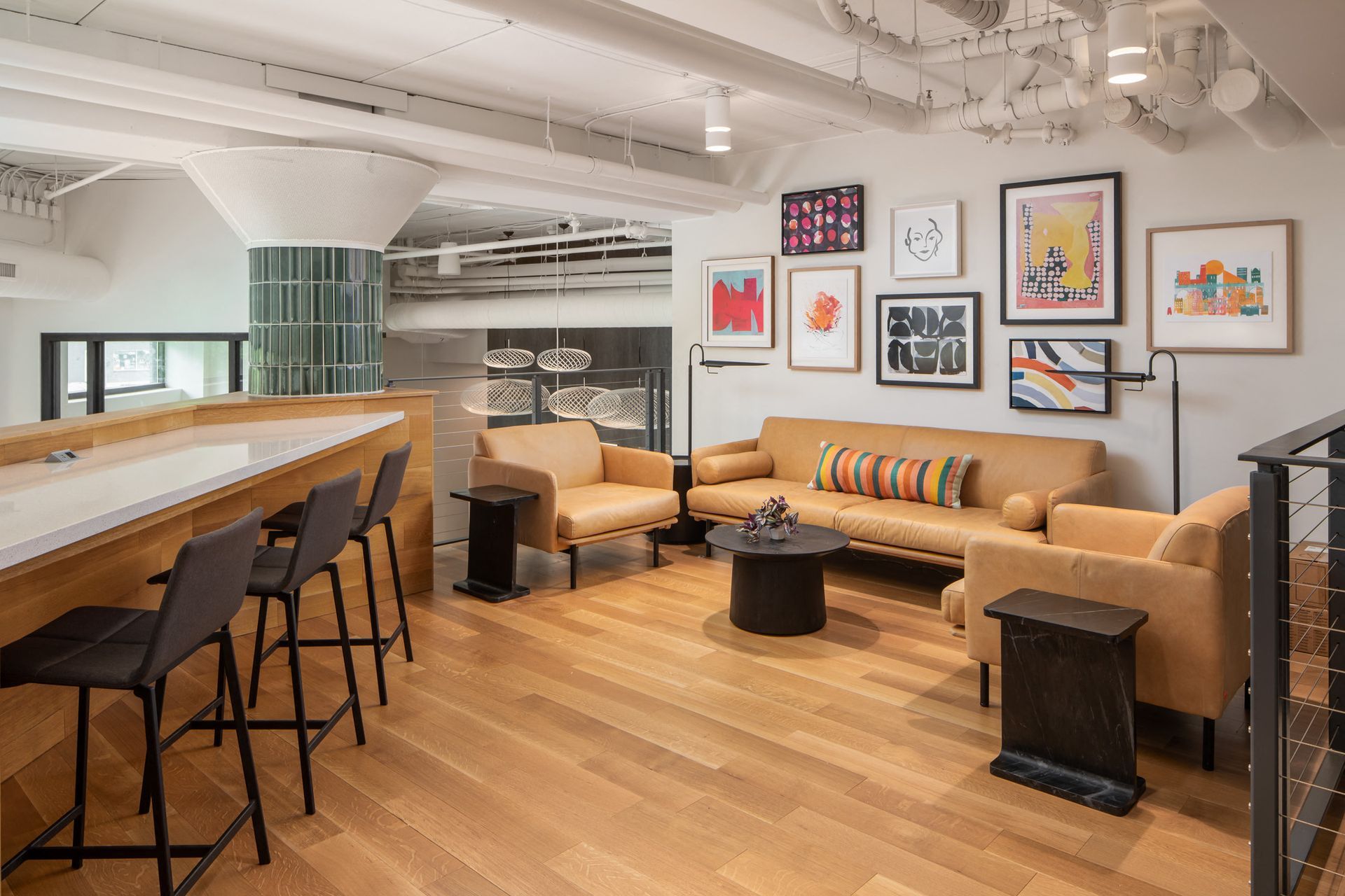 Open-plan resident lounge with tan sofas, a coffee table, bar seating, and art-filled wall.