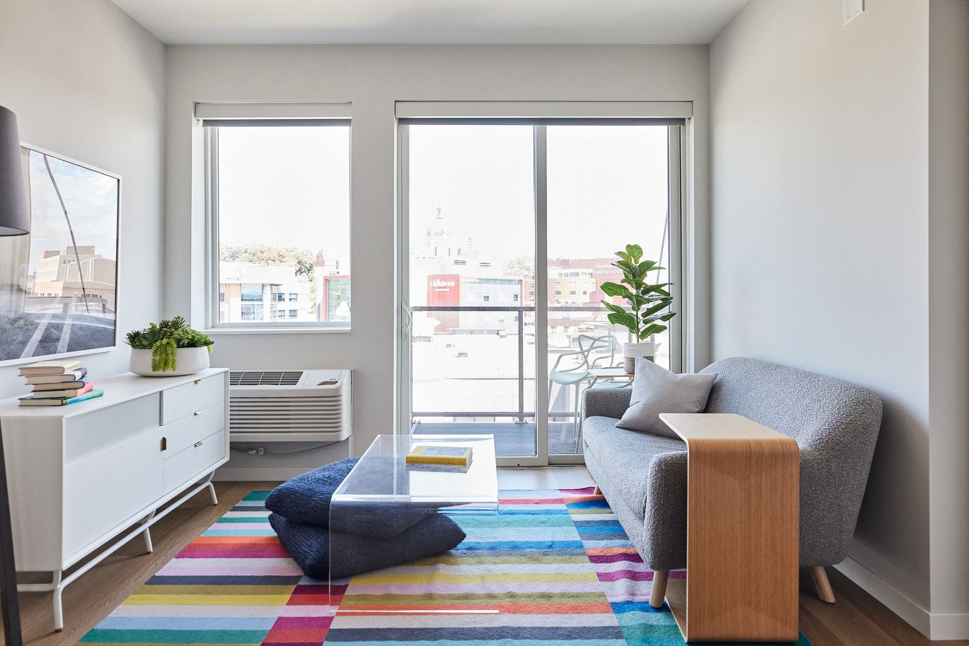 Bright living room with a colorful striped rug, gray sofa, and balcony doors.