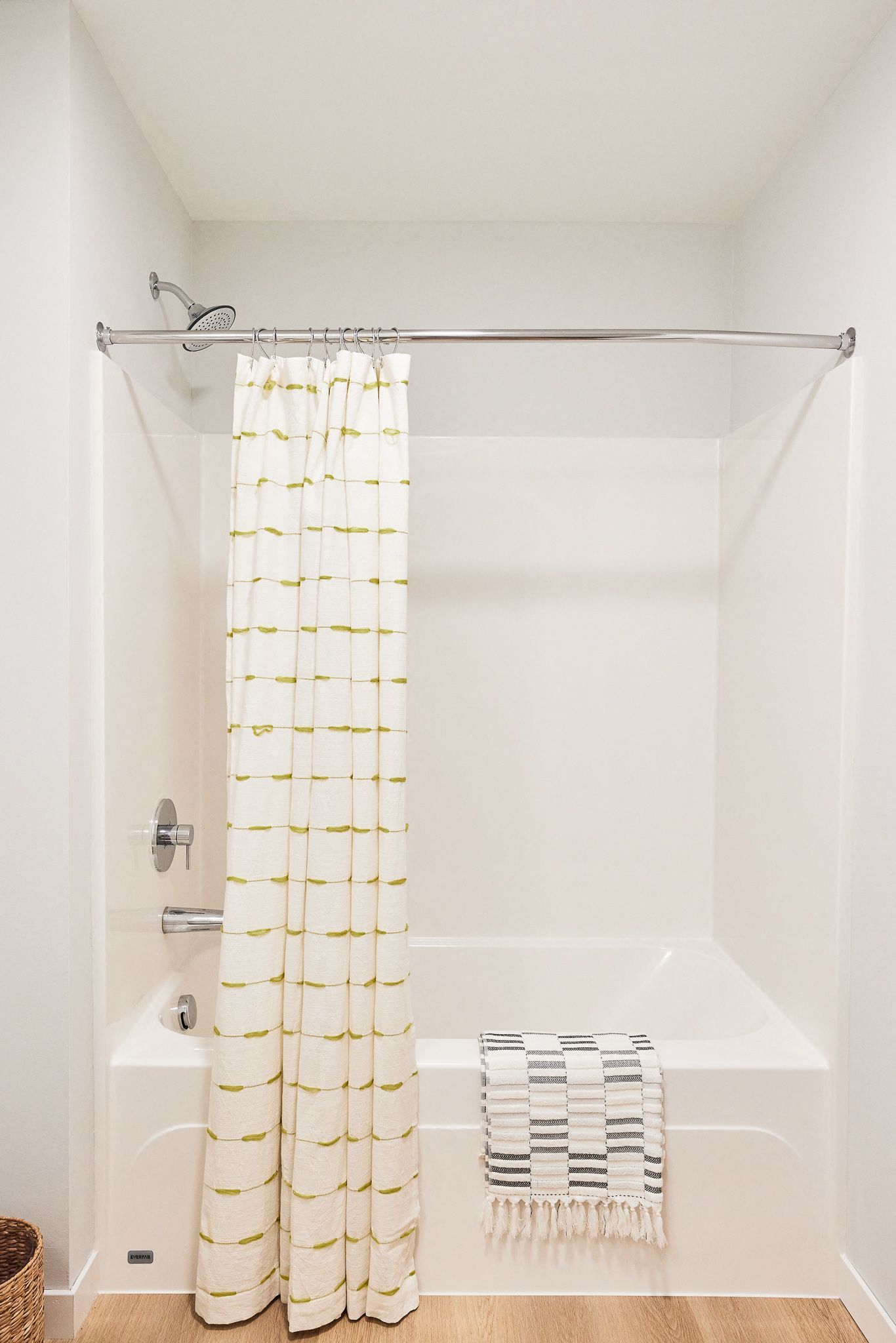 Bathroom shower with white tile, chrome fixtures, and a cream shower curtain with green lines.