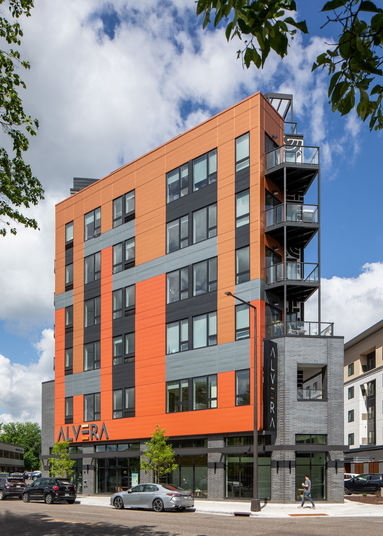 Modern multifamily building exterior with orange and gray panels and balconies.