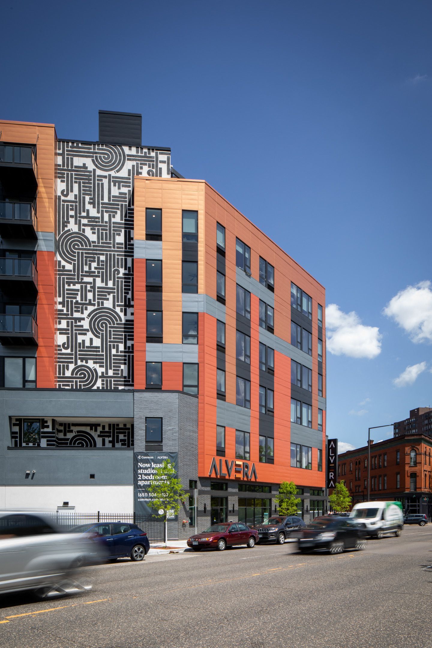 Exterior view of a modern apartment building with orange panels and a black-and-white geometric mural.