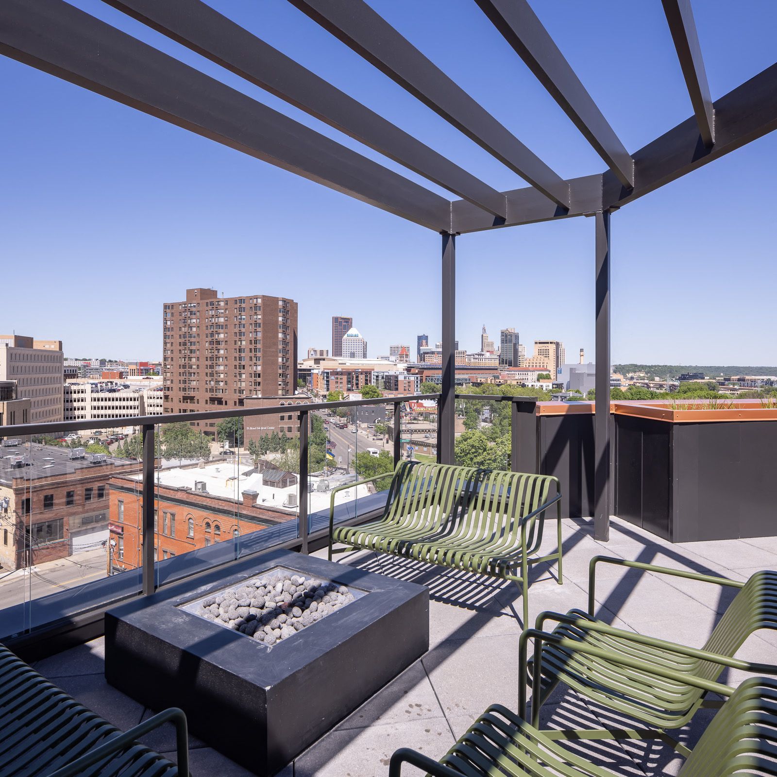 Rooftop amenity terrace with green chairs, fire pit, and city skyline view.