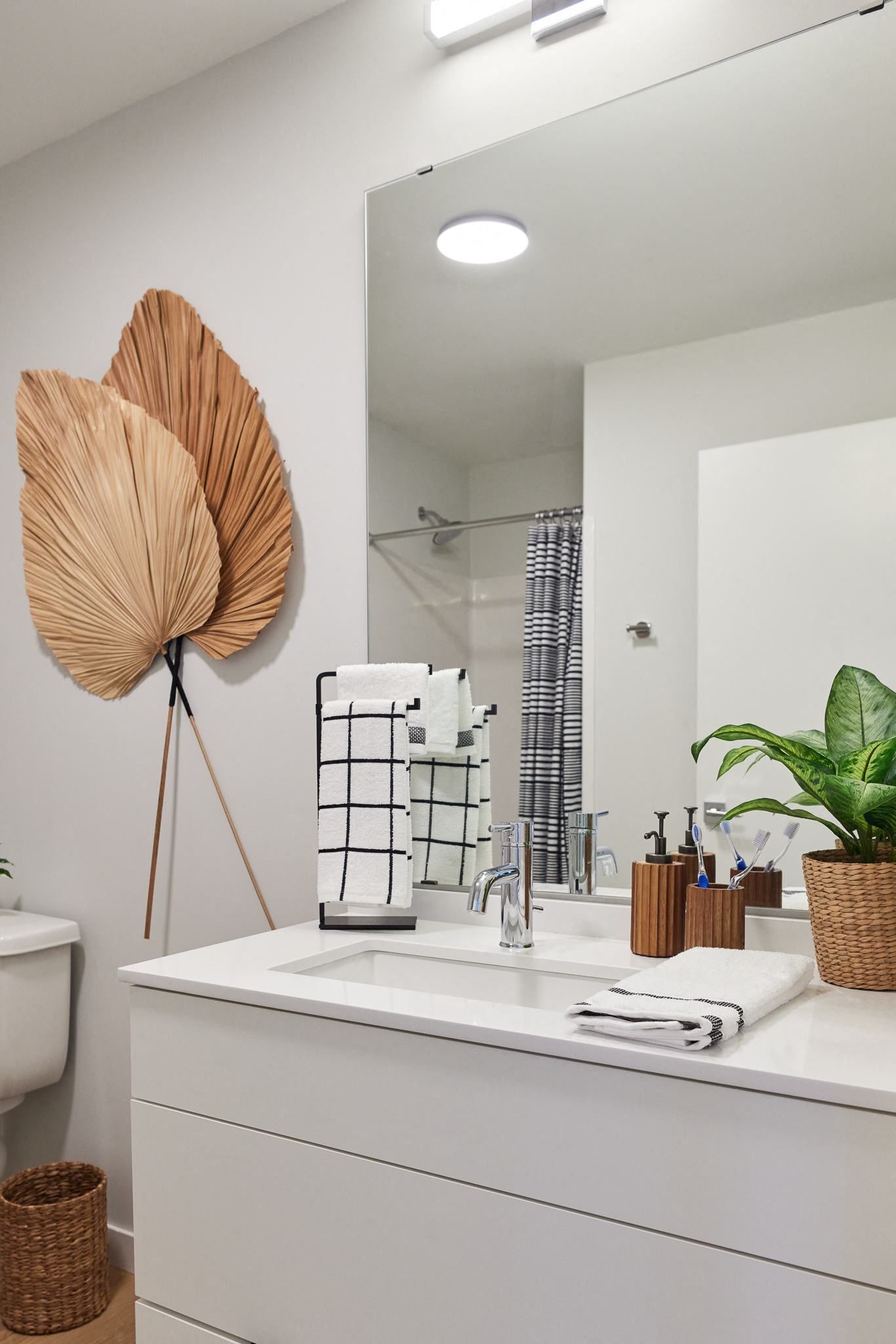 Bright bathroom with a white vanity, large mirror, towels, and a decorative palm leaf sculpture.
