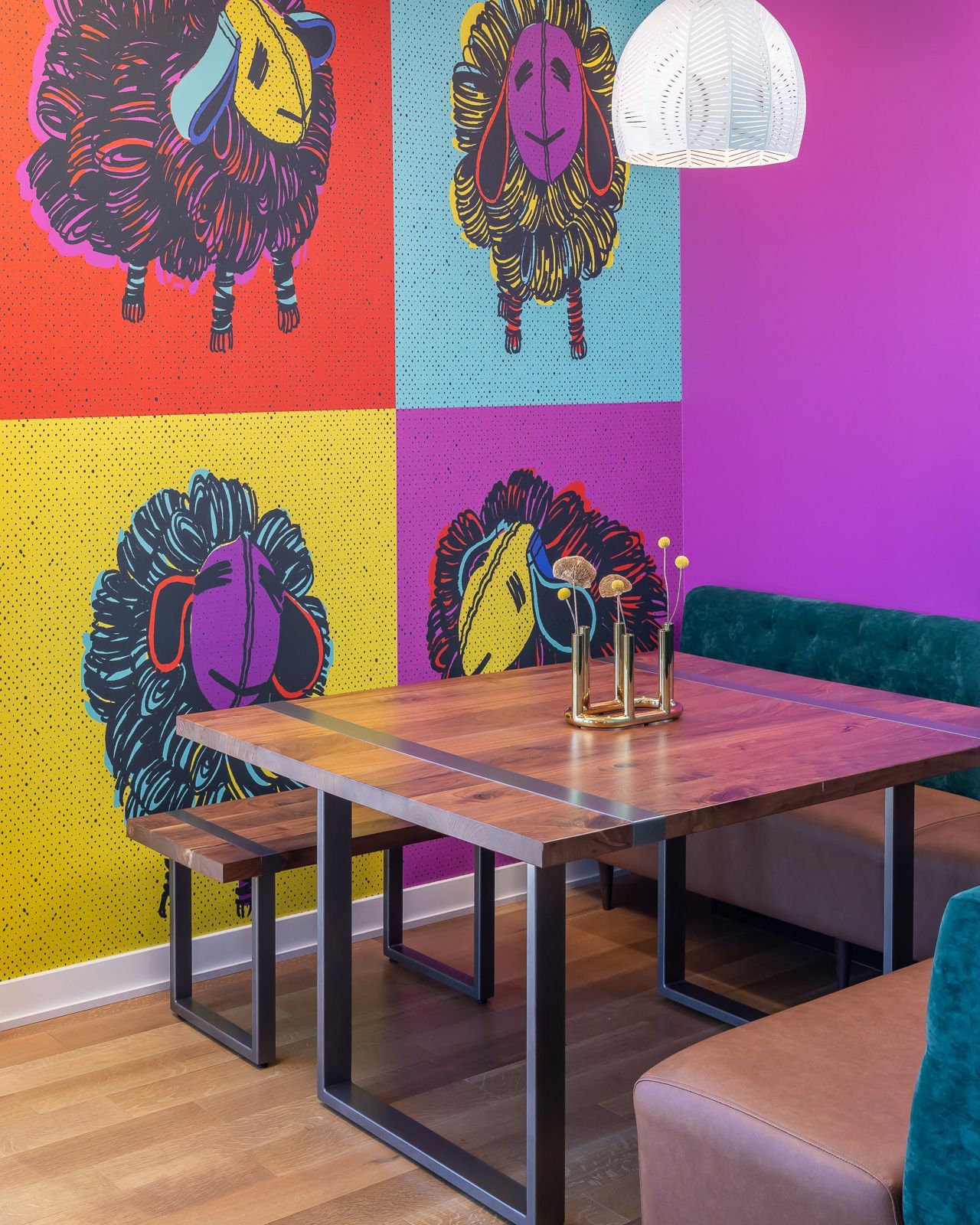 Communal dining lounge with a large colorful wall mural and wooden table.