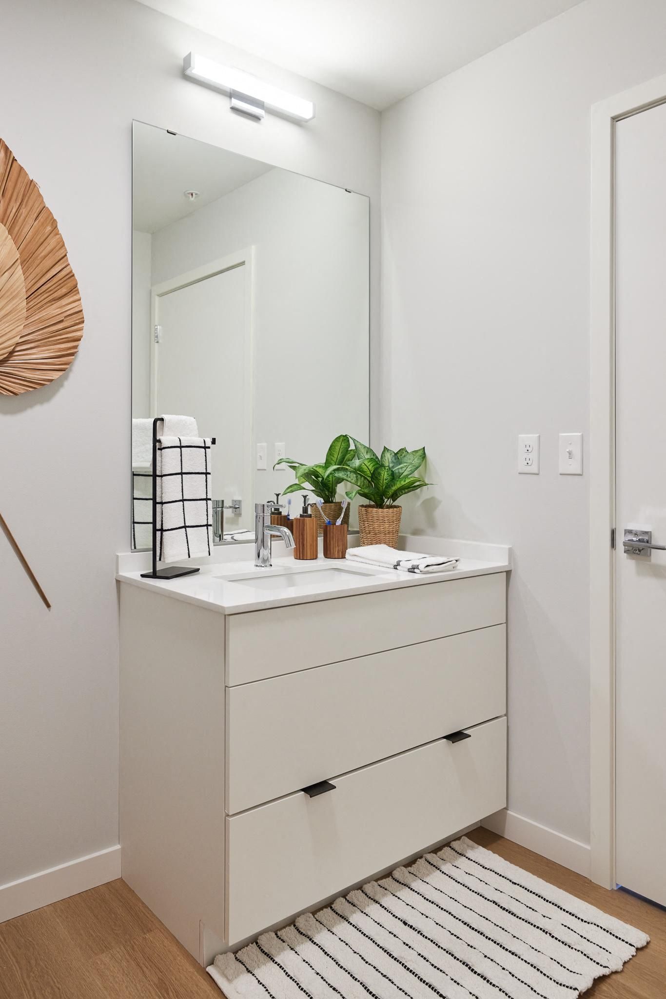 White bathroom vanity with sink, large mirror, plant, towels, and striped rug.
