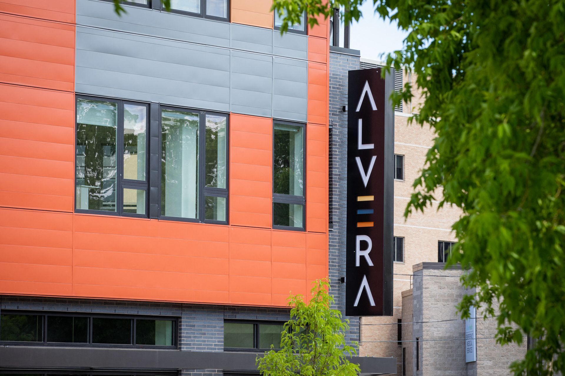 Exterior view of a modern apartment building with orange panels and a tall vertical sign.