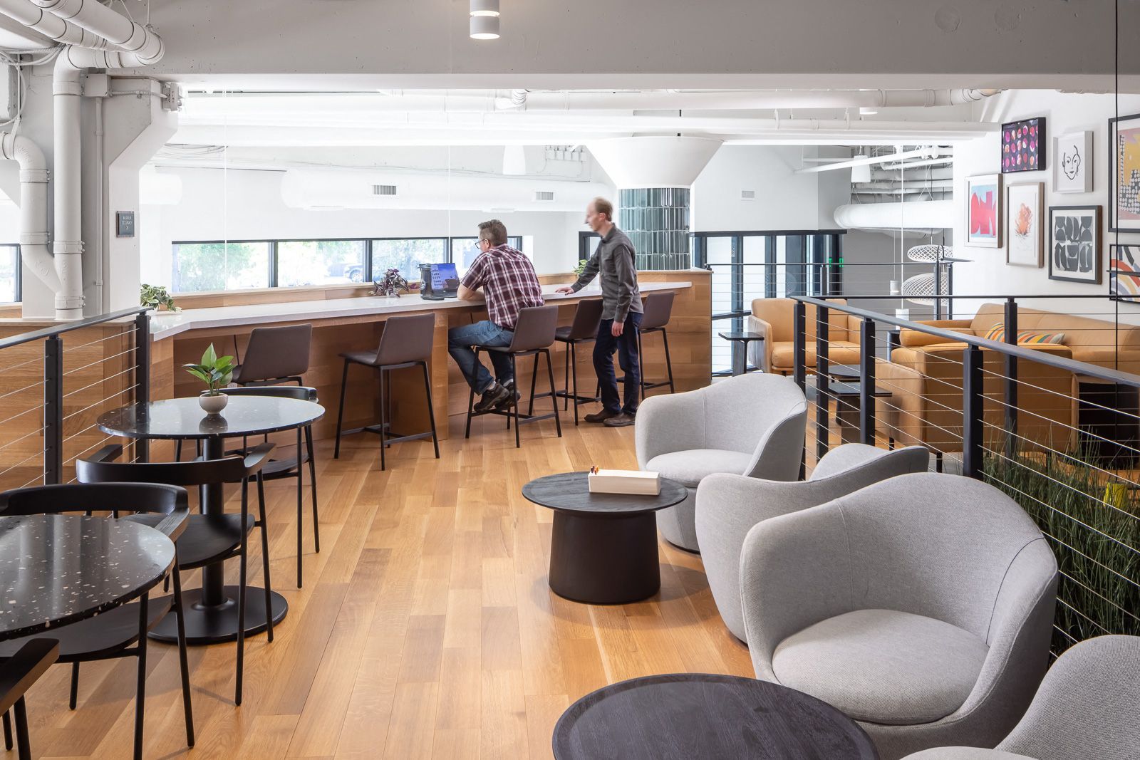 Open indoor lounge with wood floors, a long bar-style counter, and gray seating; two people at the counter.