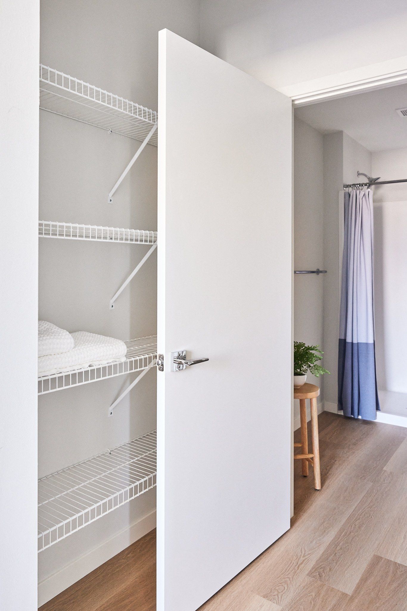 Open white closet with wire shelves beside a bathroom with a blue shower curtain.