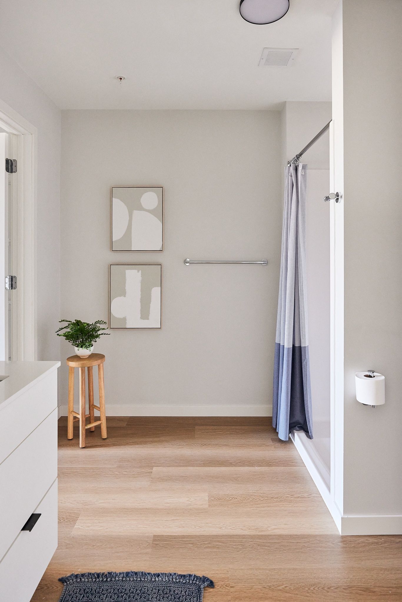 Modern apartment bathroom with a shower, light gray walls, and a wooden floor.