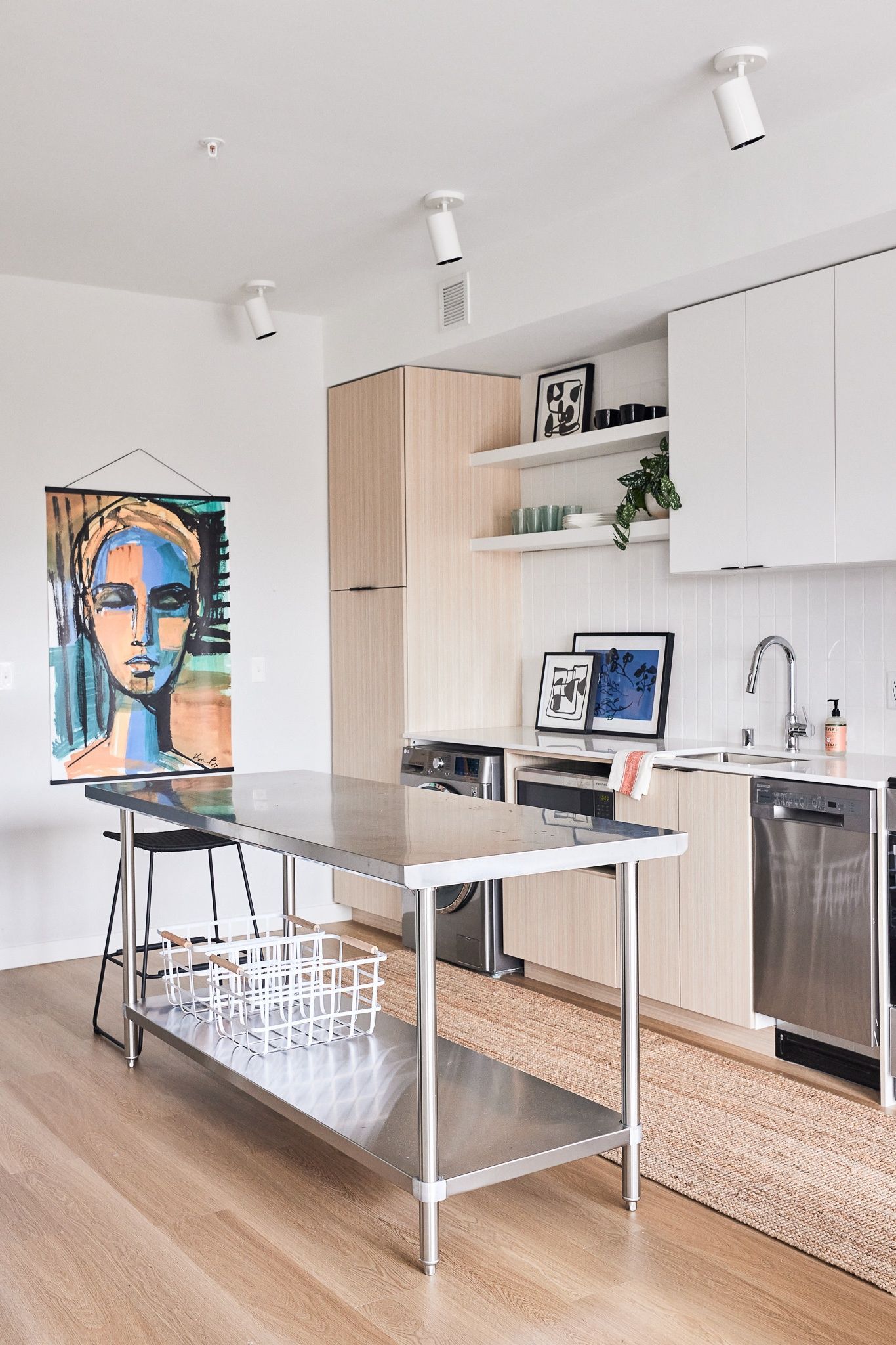 Modern apartment kitchen with stainless steel island, white cabinets, and open shelving.