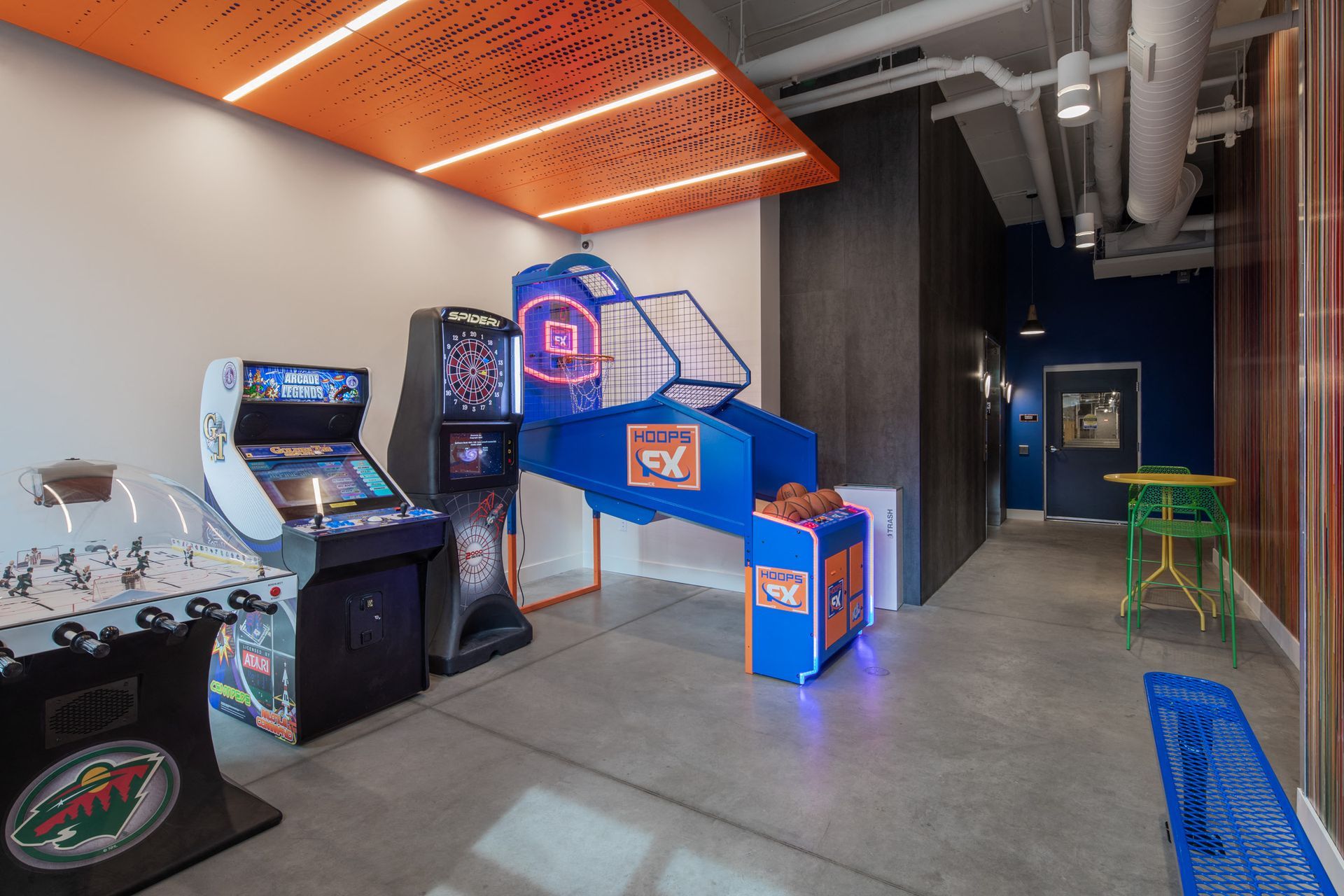 Indoor recreation room with arcade games, a basketball arcade, and colorful seating near a blue doorway.