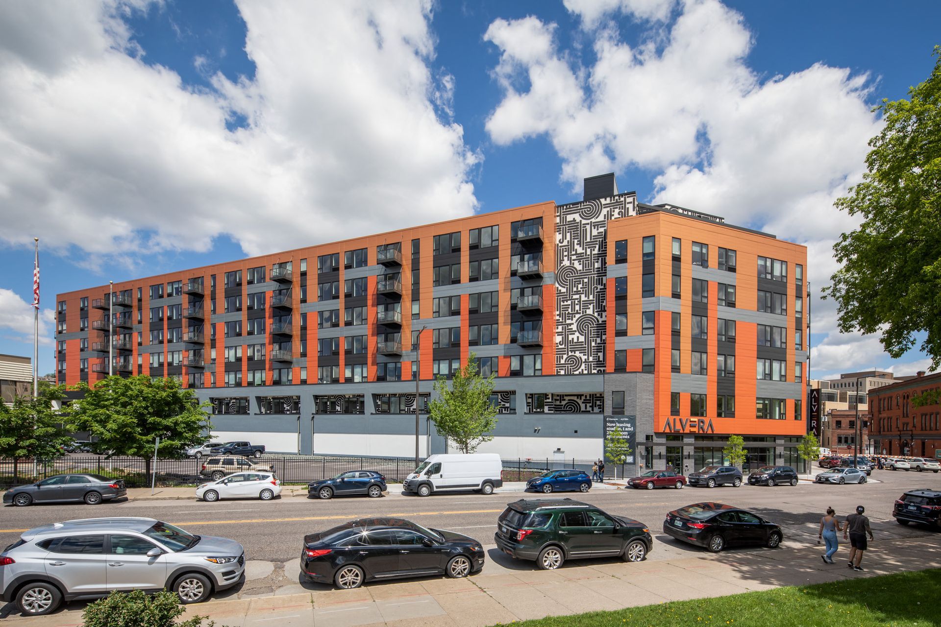 Exterior view of a modern orange-and-gray apartment building along a street.