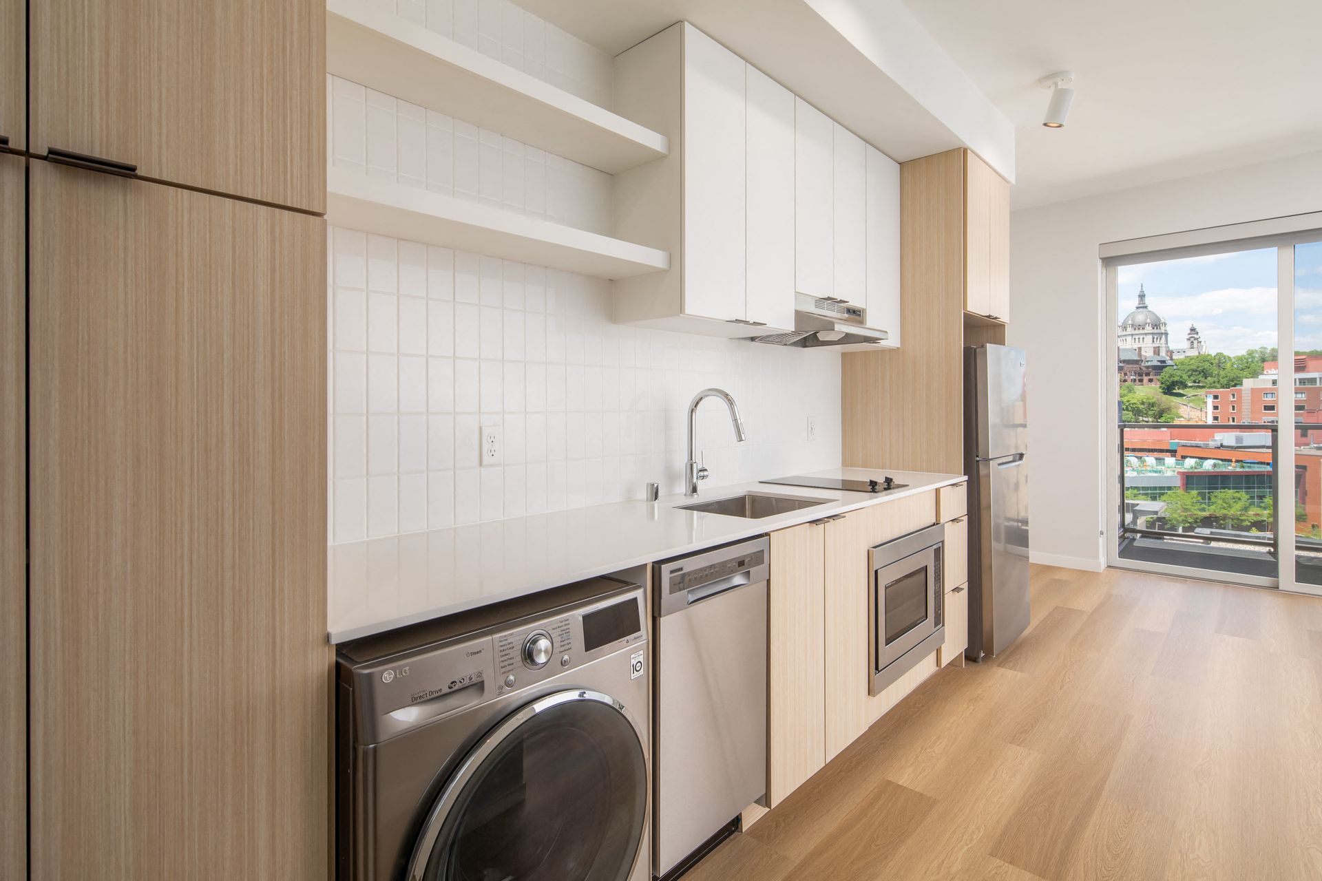 Modern apartment kitchen with white cabinets, stainless appliances, and a balcony view.