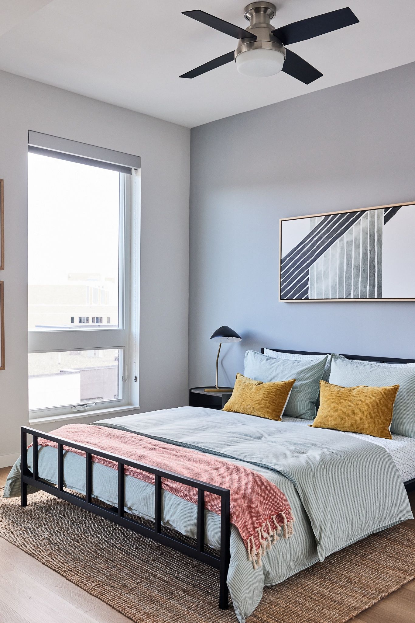Bedroom with a black metal bed frame, pale blue bedding, a rug, and a ceiling fan by a large window.
