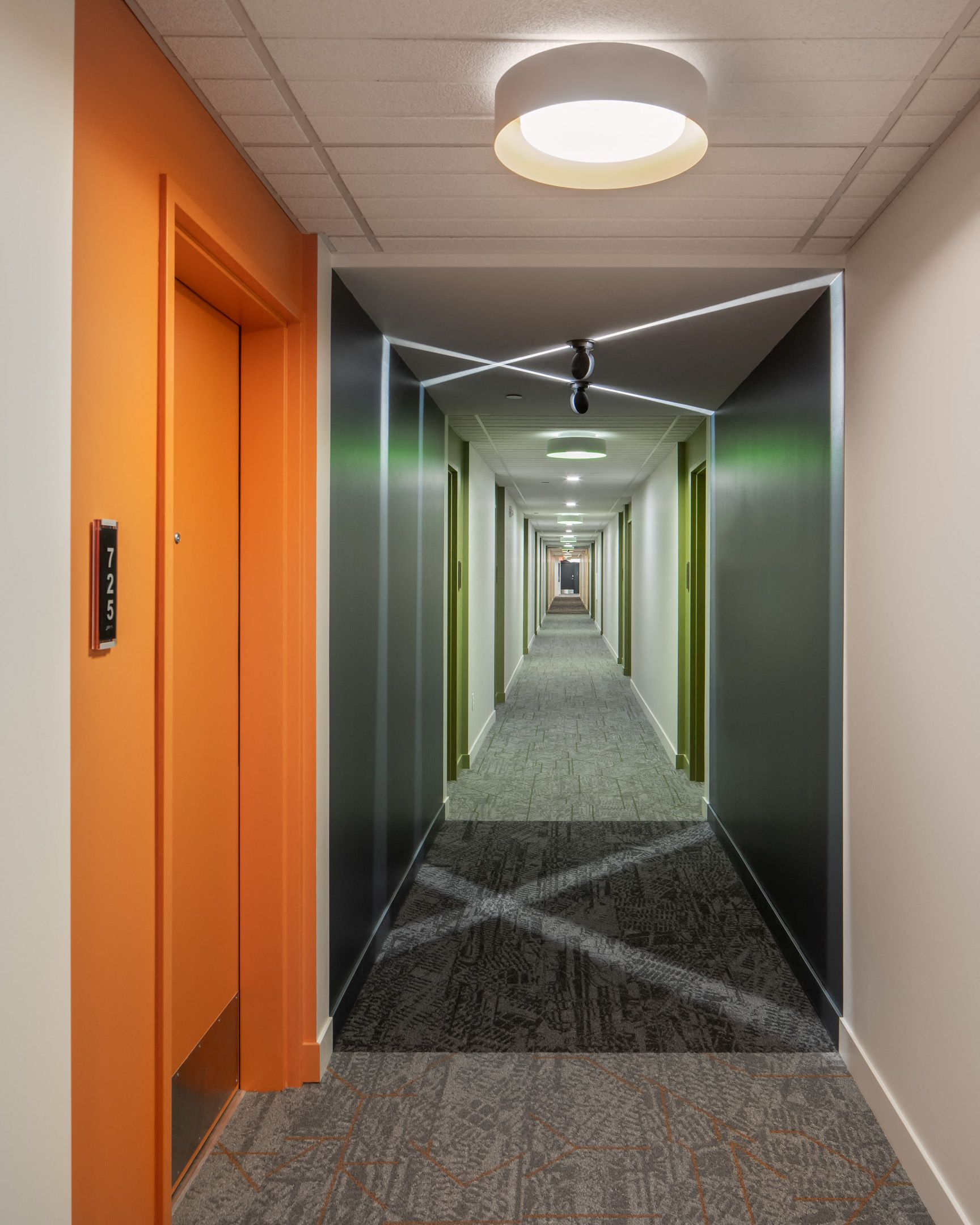 Interior hallway inside an apartment building with an orange door frame on the left and a long, lit corridor.
