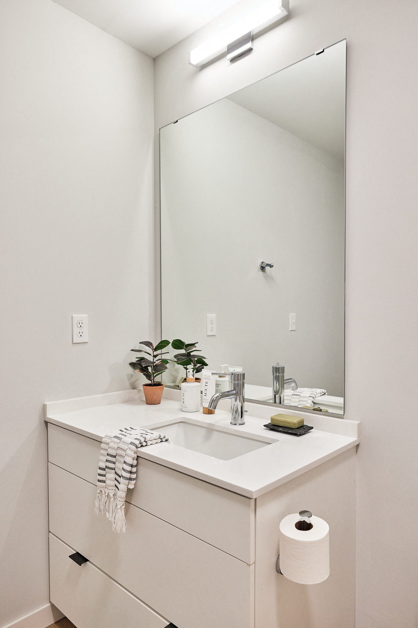 White bathroom vanity with sink, chrome faucet, large mirror, and a small plant.