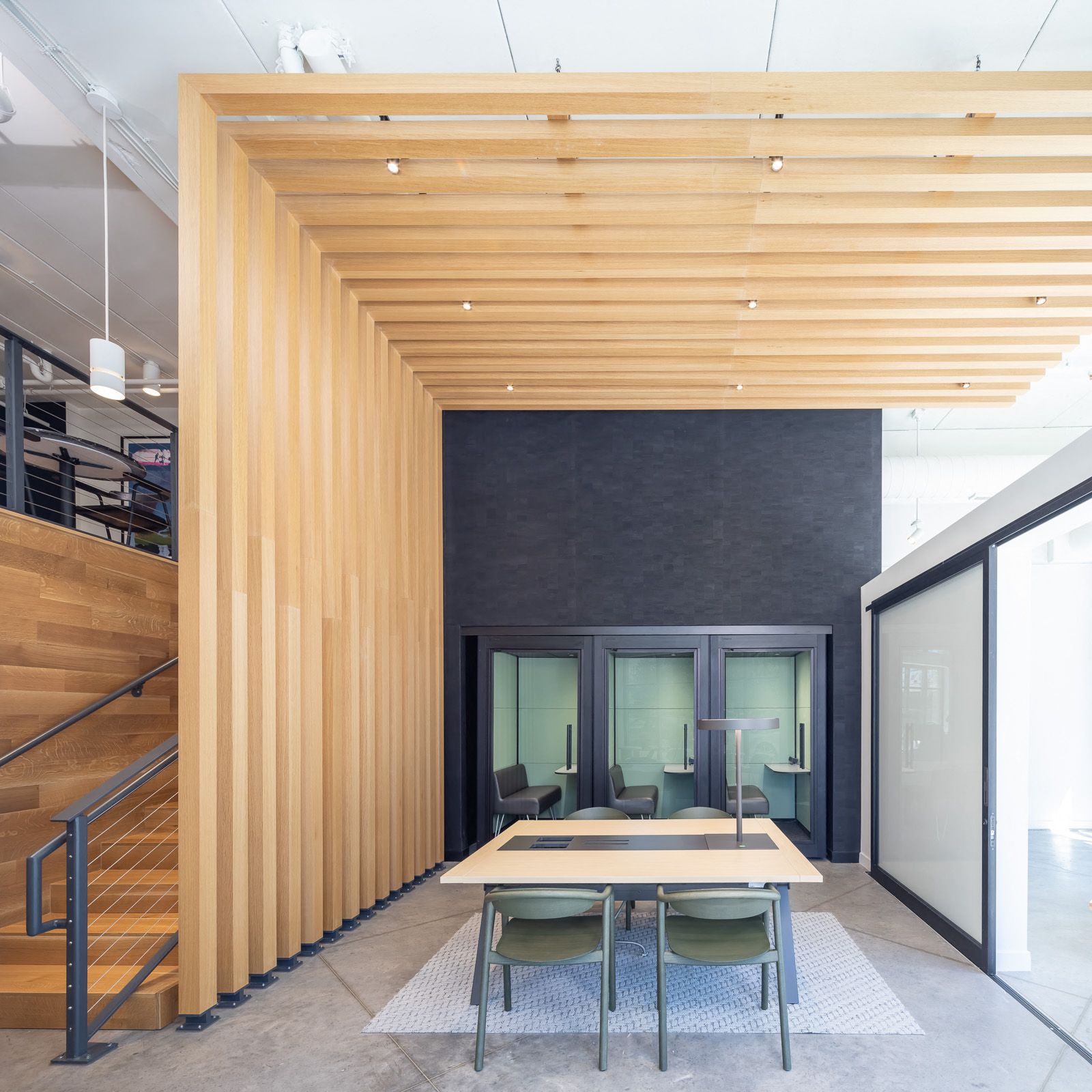 Modern community space with a wooden slatted ceiling, glass-walled meeting rooms, and a central table.