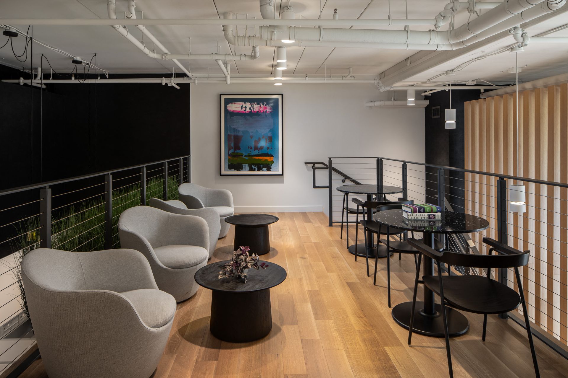 Mezzanine-style resident lounge with gray upholstered chairs, black round tables, and railing overlooking lower level.