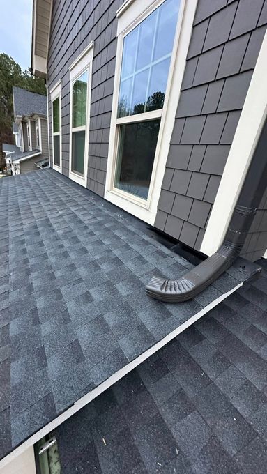 A dark grey shingled roof meets the side of a building with matching square shingles and three windows.