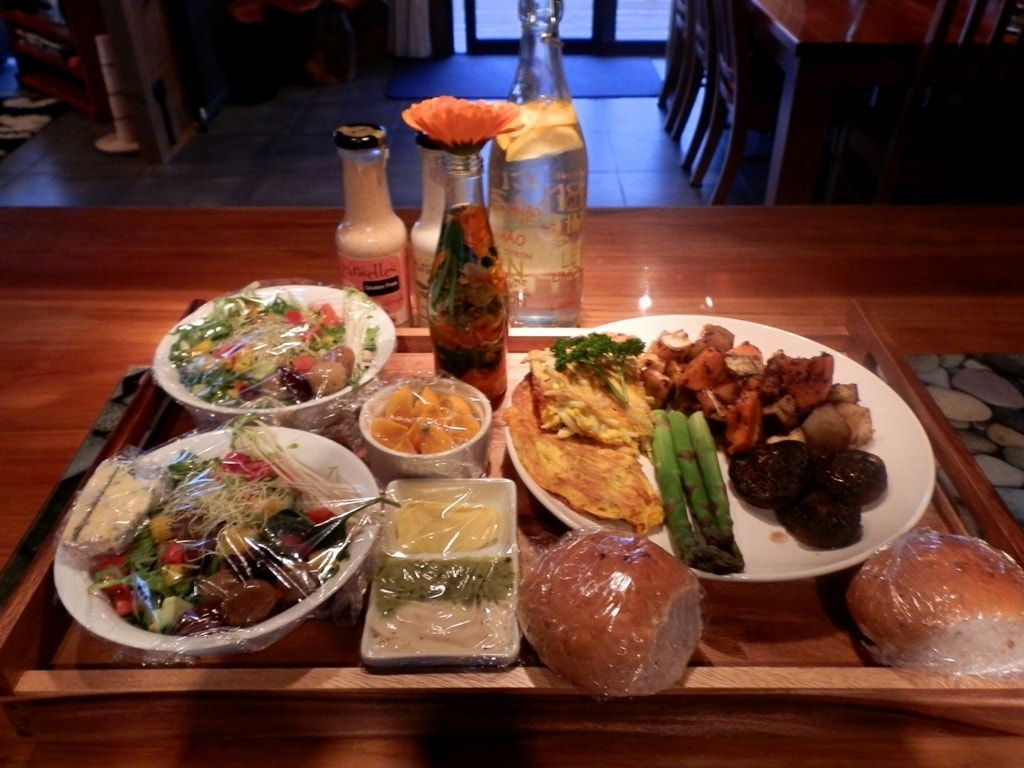 A tray with a meal: salad, vegetables, bread, condiments, water, and orange flower.