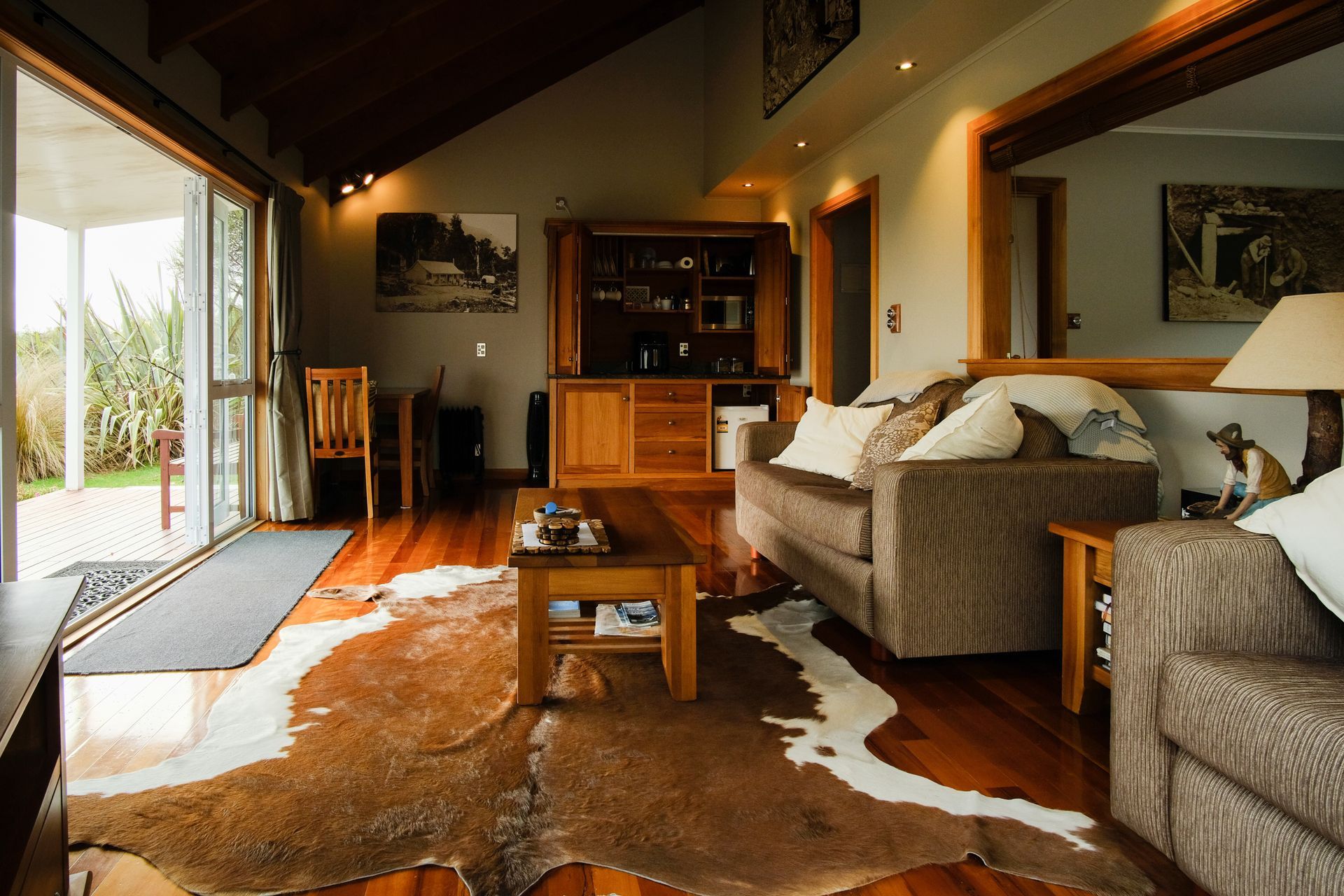 Living room with cowhide rug, brown sofa, wooden furniture, and open doors to a garden.