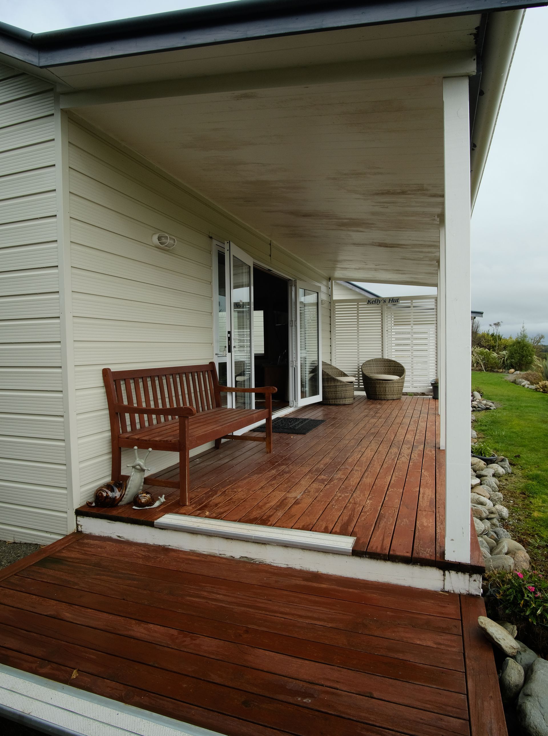 Wooden deck with bench and glass doors, extending from a cream-colored house.