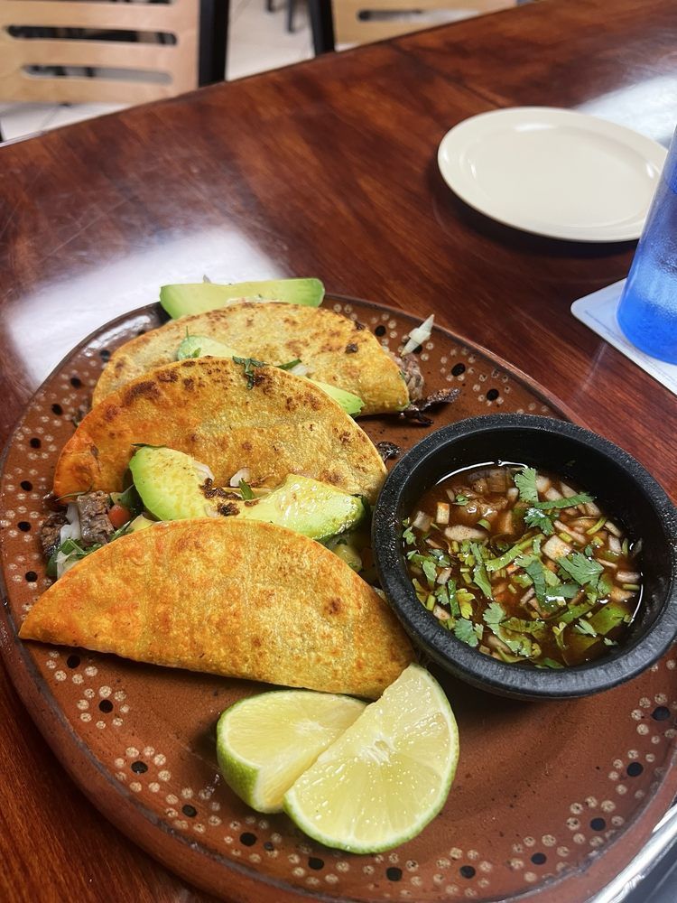 Plate of tacos with avocado, lime, and dipping sauce.