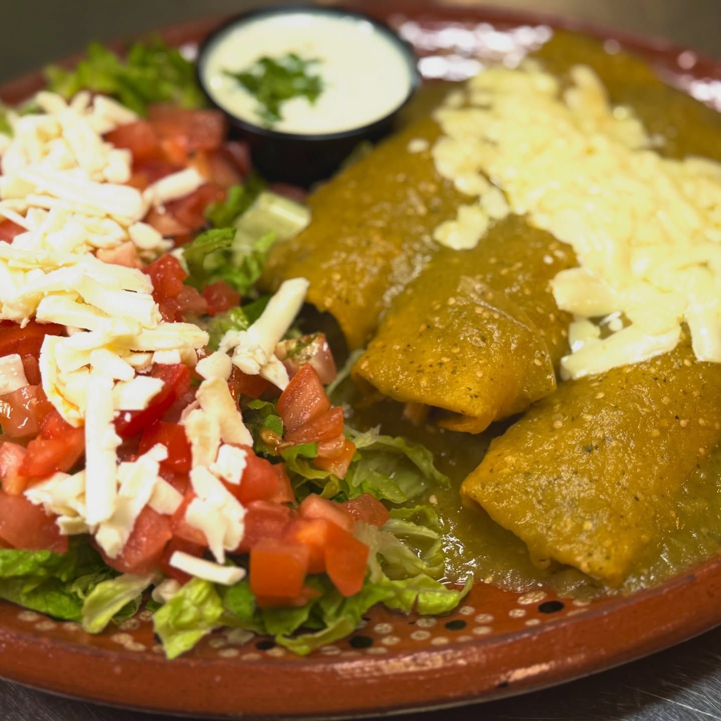 Enchiladas covered in green sauce, topped with cheese, served with salad and sour cream.