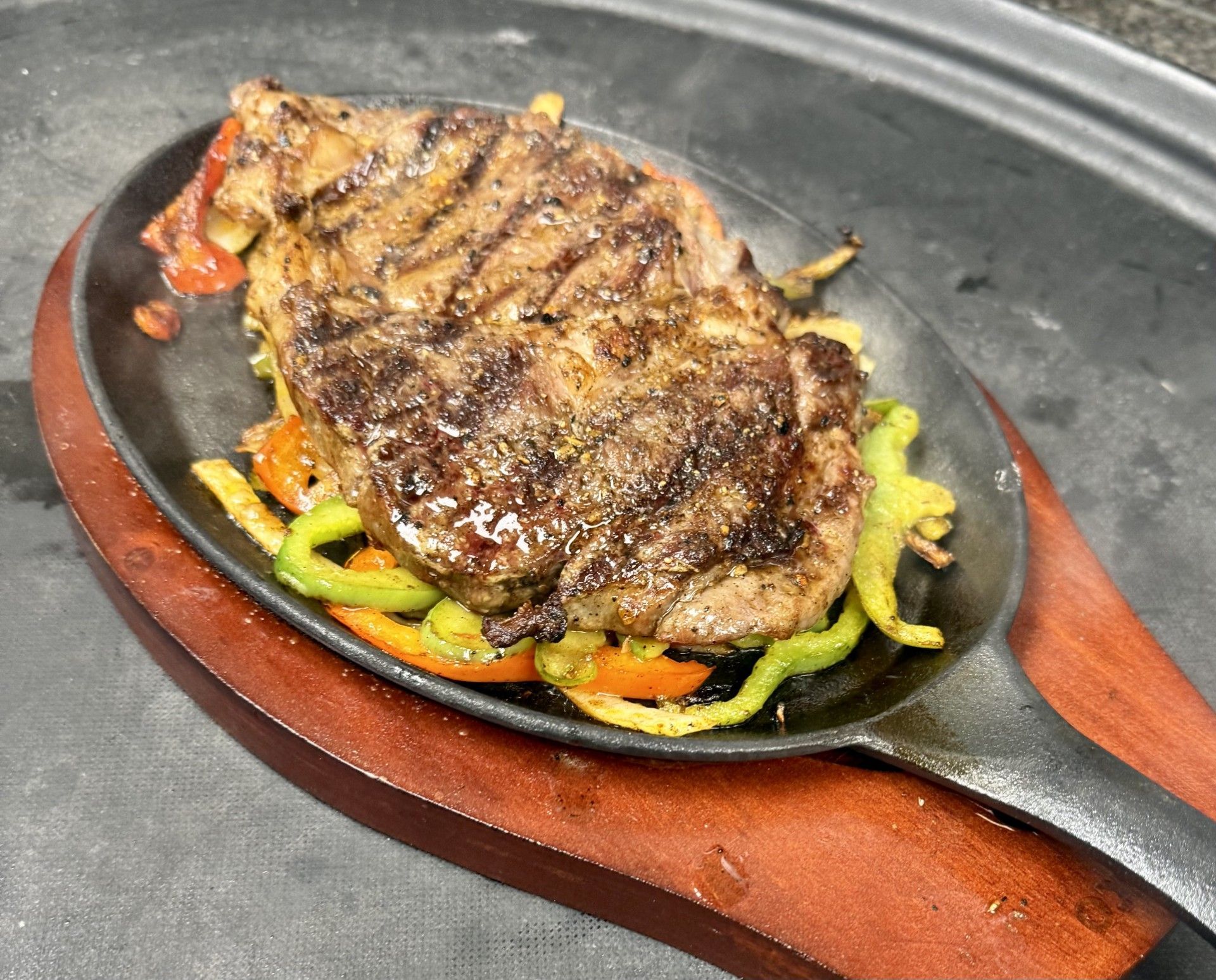 Grilled steak on a bed of peppers, served in a cast iron skillet on a wooden base.