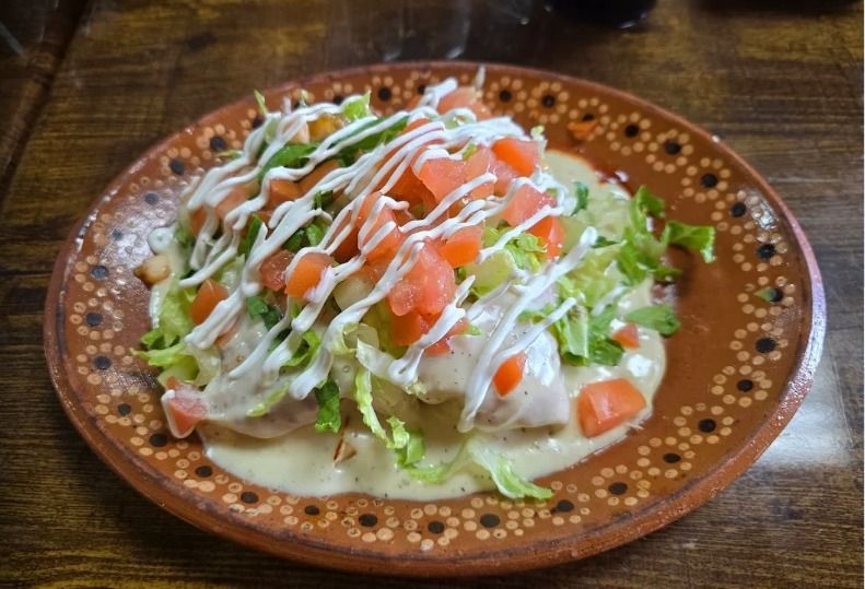 Mexican dish: tostadas with creamy sauce, lettuce, diced tomatoes, and white drizzle, served on a decorated brown plate.