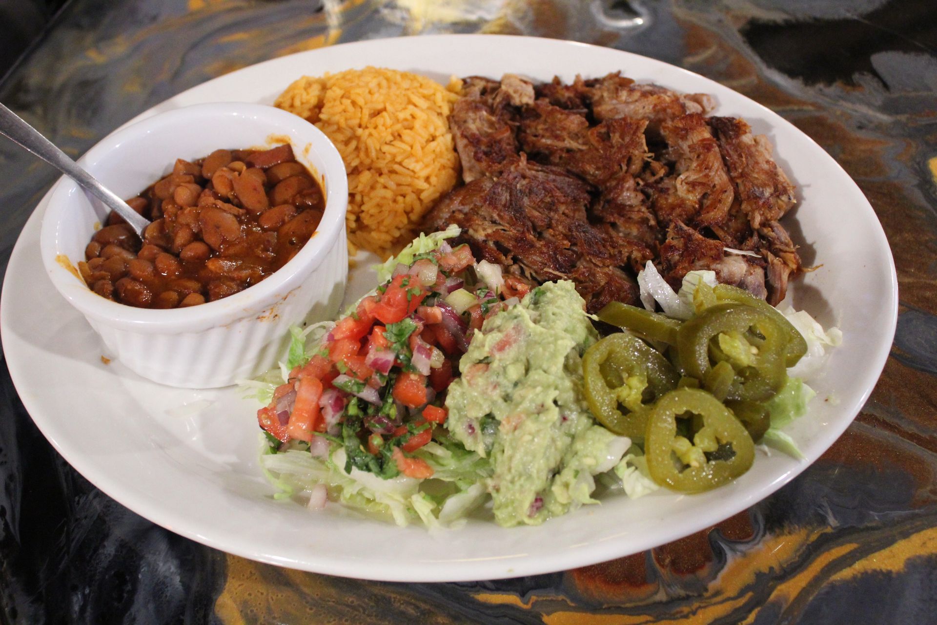 Plate of Mexican food: steak, rice, beans, salsa, guacamole, jalapeños.
