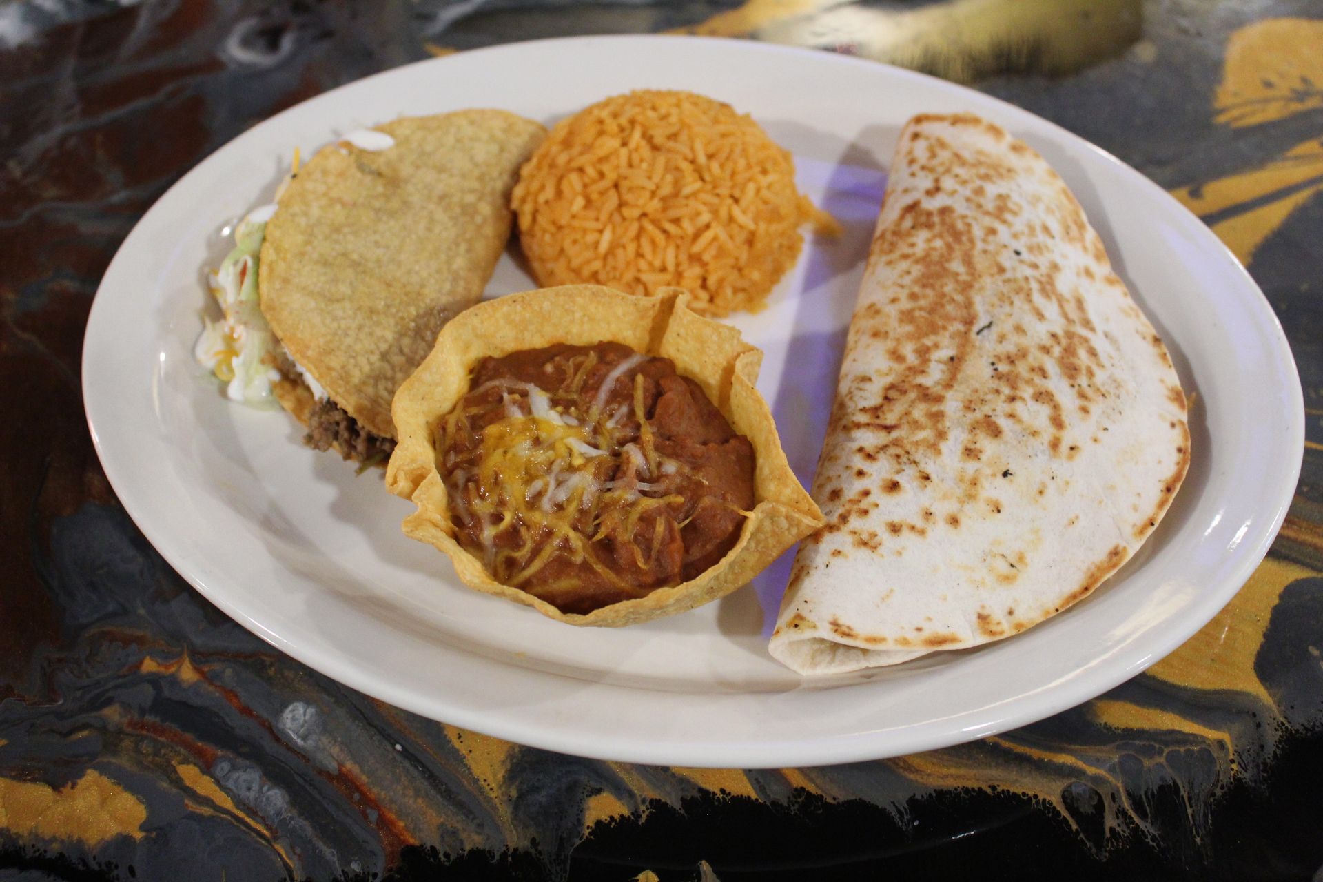 Plate of Mexican food: taco, tortilla, rice, beans in a crispy shell.