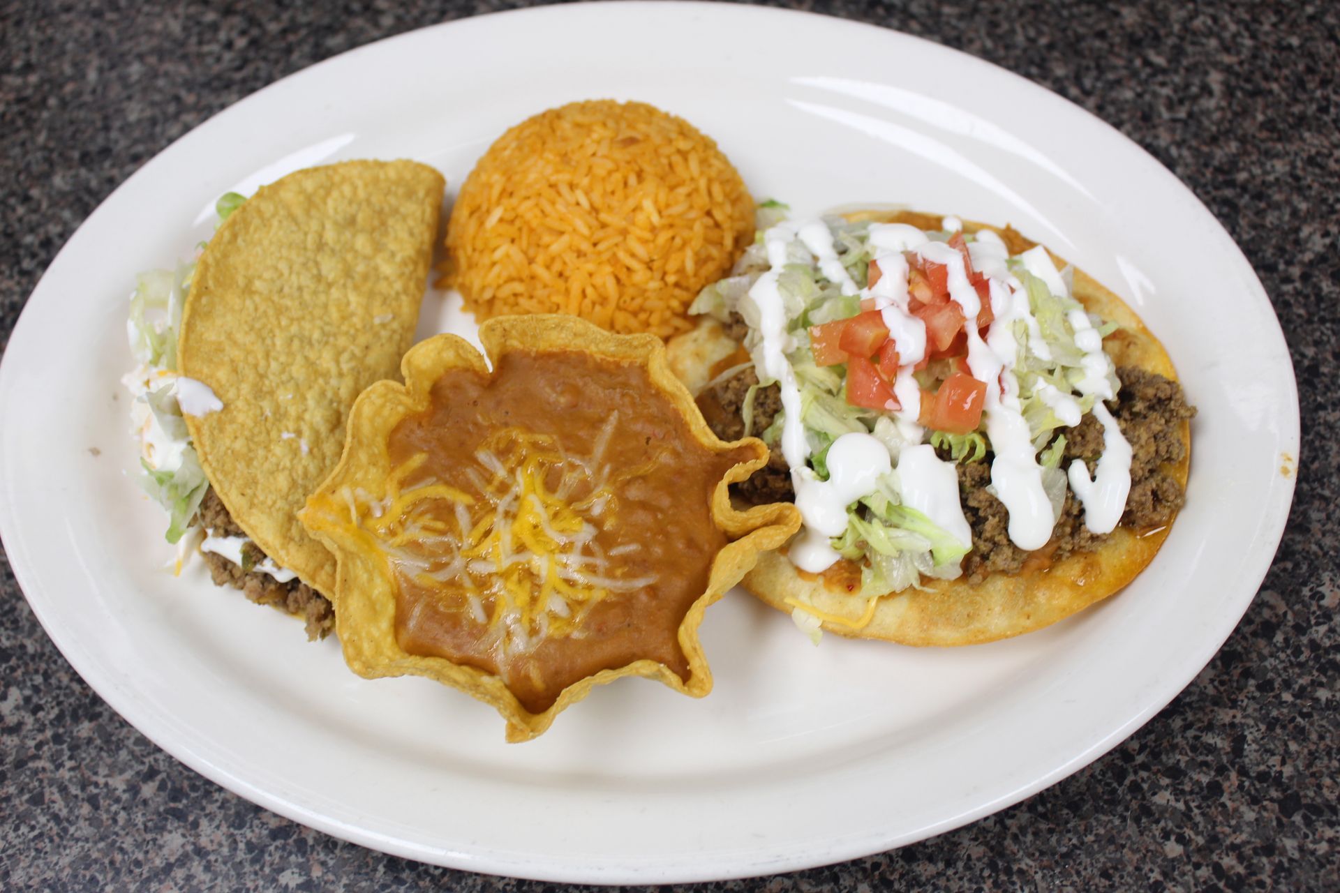 Plate with taco, tostada, refried beans, and rice.
