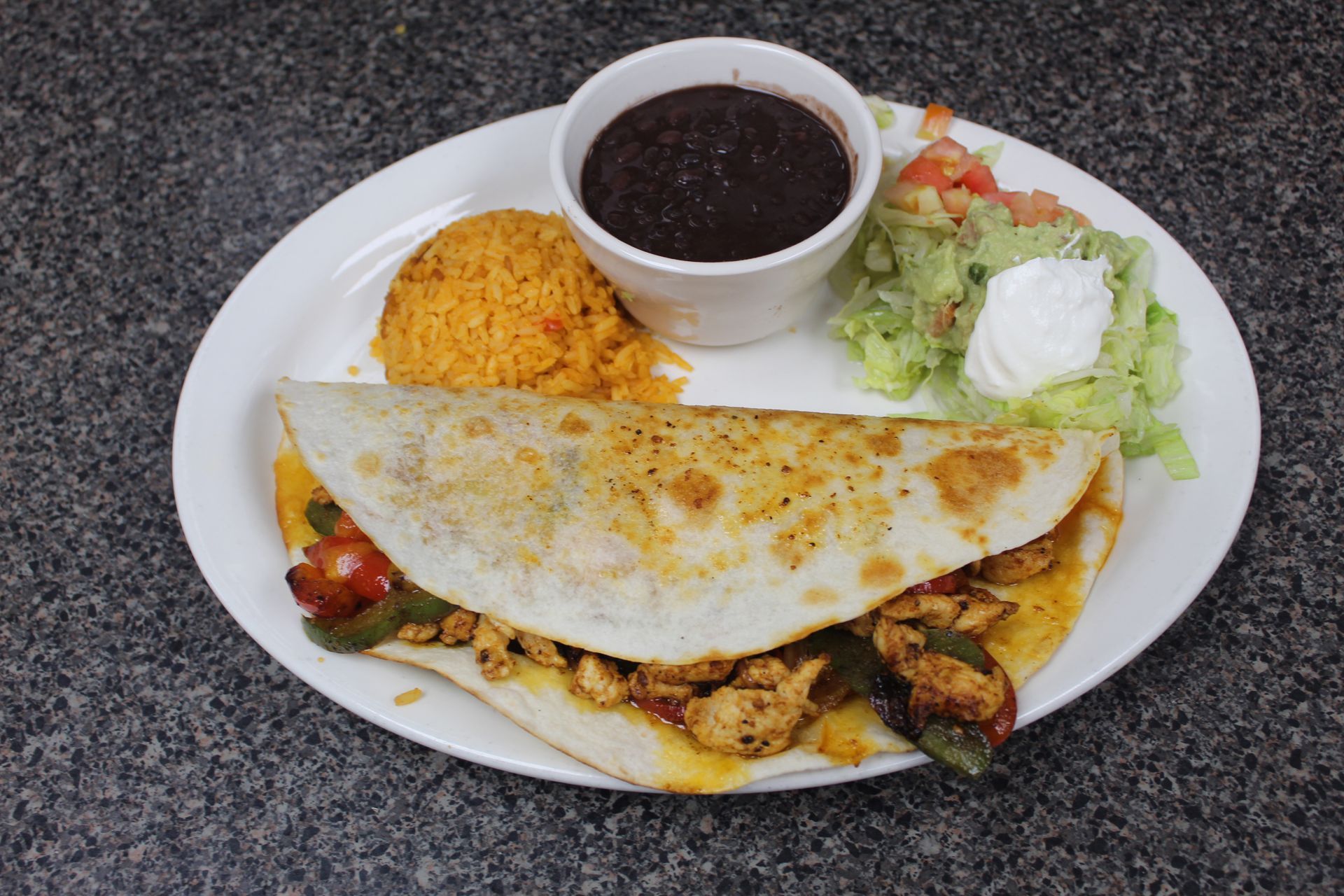 Mexican cuisine dish: chicken quesadilla, rice, black beans, salad, and sour cream.