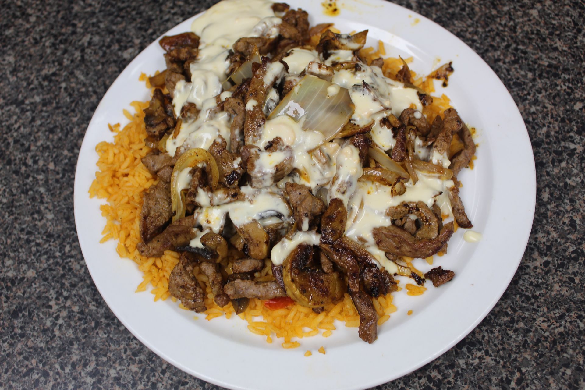 Plate of Mexican food: rice, steak, onions, and creamy sauce.