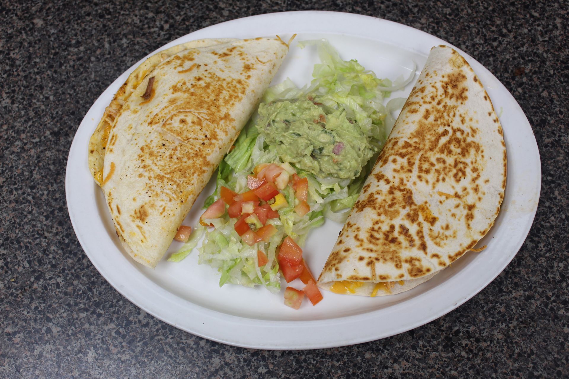 Quesadillas with guacamole, lettuce, and diced tomatoes on a white plate.