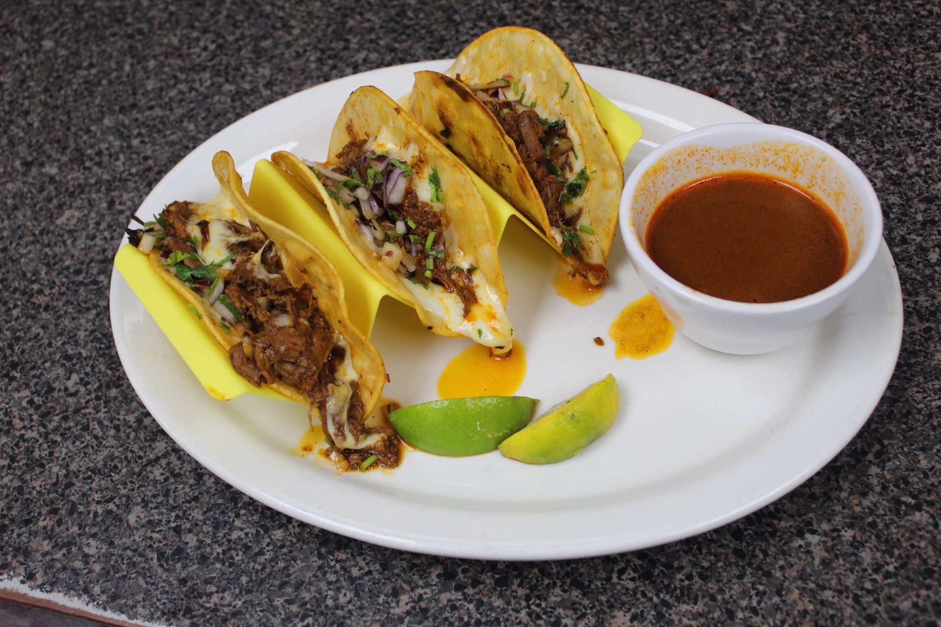 Plate of tacos with dipping sauce and lime wedges.