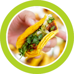 Hand holding a taco with yellow shell, meat, salsa, and cilantro, close-up with a green circle around.