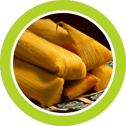 Tamales wrapped in corn husks, piled on a patterned plate.