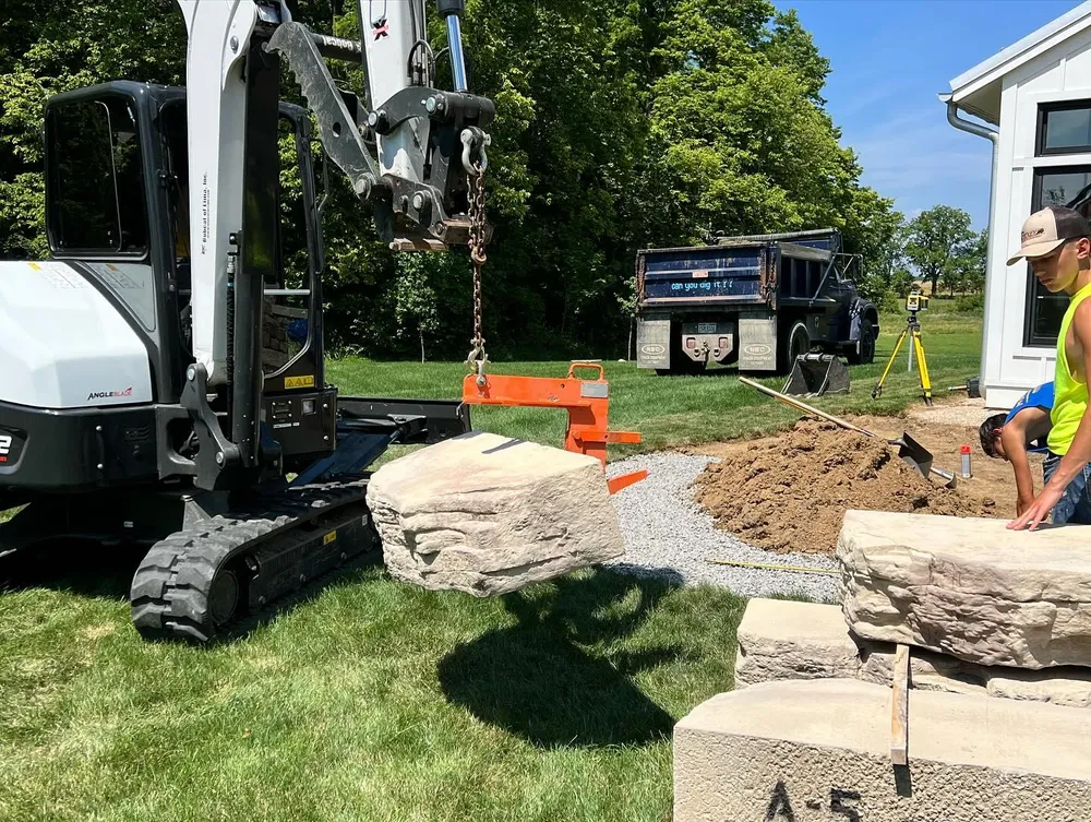 A bulldozer is lifting a large rock in a yard.