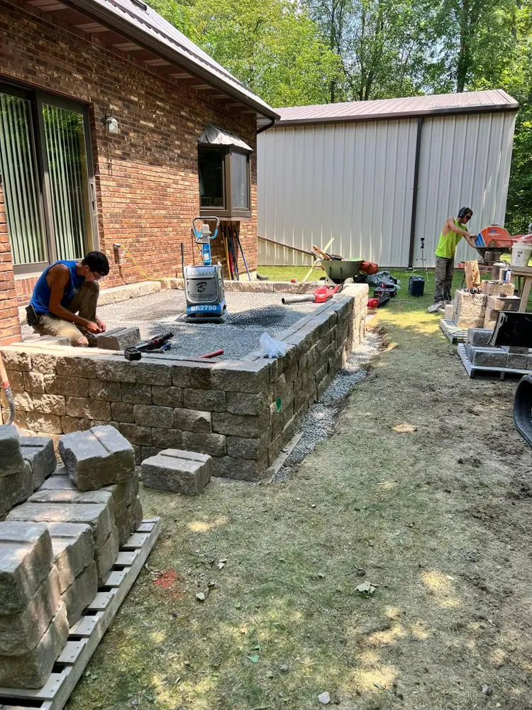 A man is laying bricks on a patio in front of a brick house.