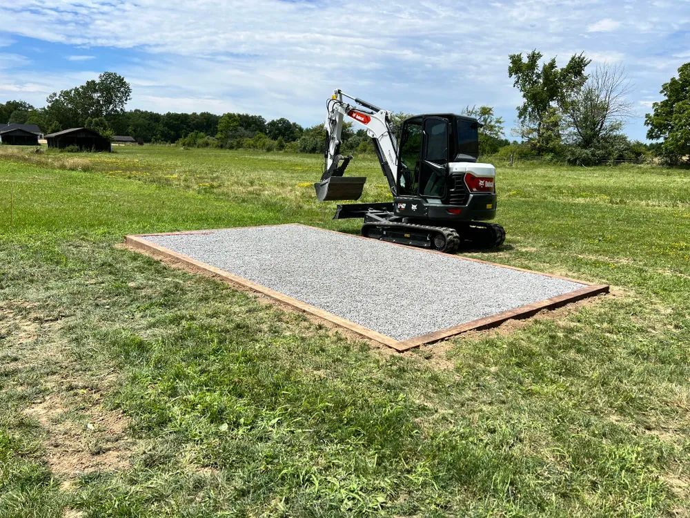 A small excavator is digging a hole in the grass in a field.