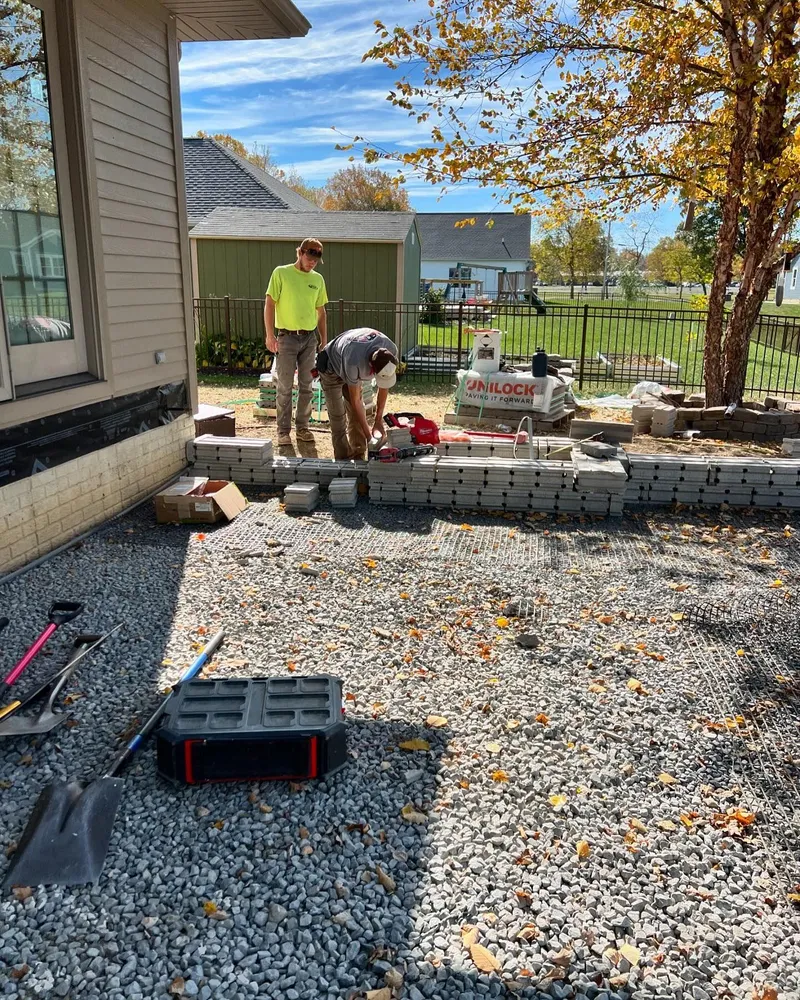 Two men are working on a patio in front of a house.