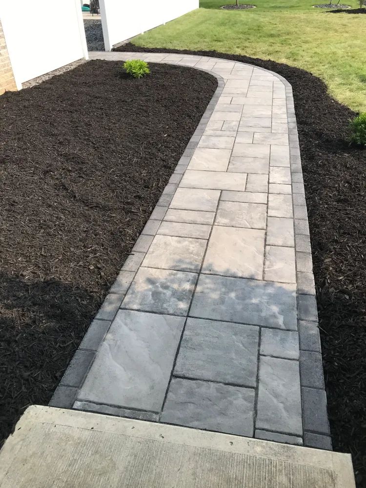 A brick walkway leading to a house with black mulch on the side.