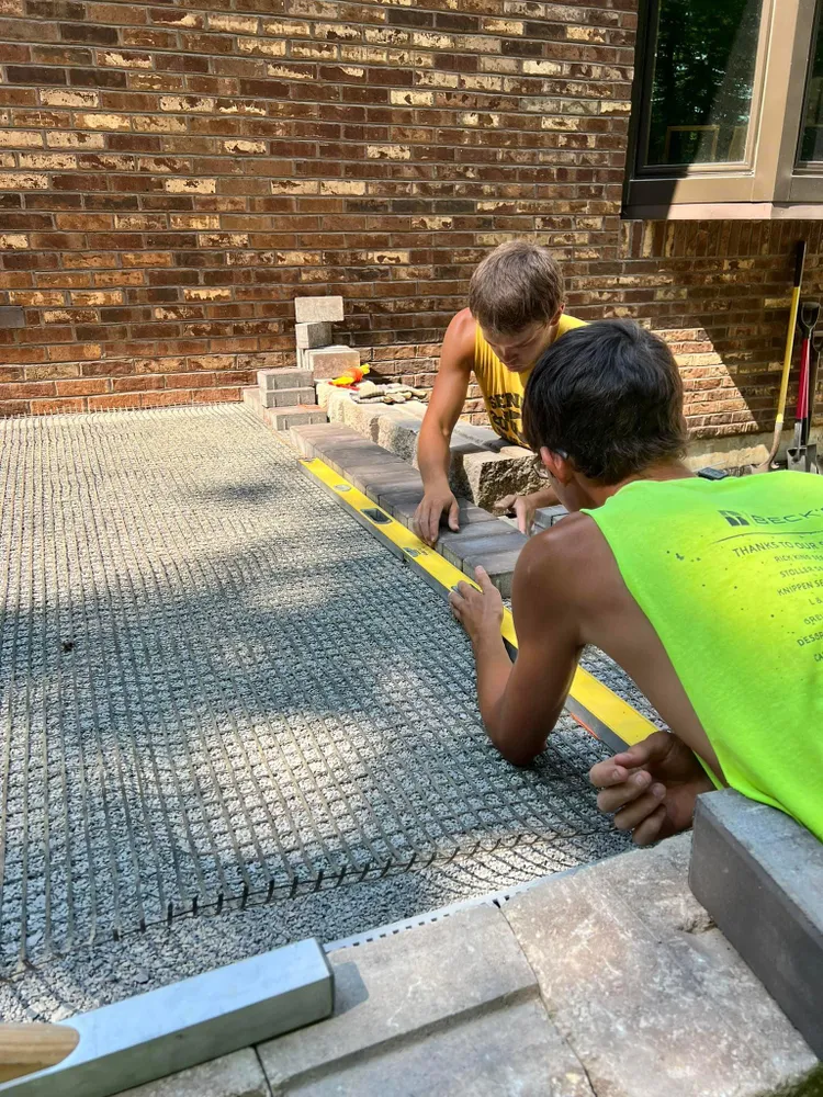 A couple of men are working on a brick patio.