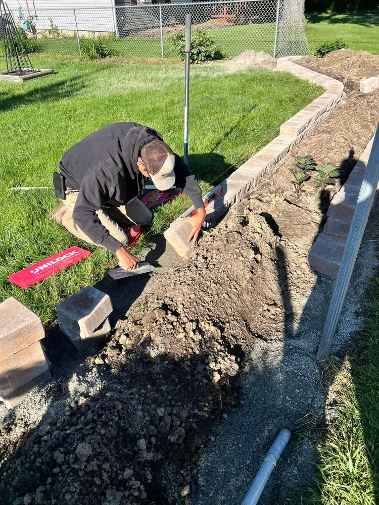 A man is laying bricks on a sidewalk in a yard.