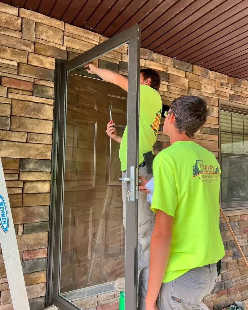 Two men in neon green shirts are cleaning a door.
